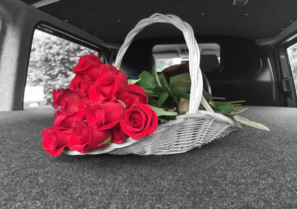 Panier en osier blanc garni de roses rouges à l'arrière d'un véhicule funéraire